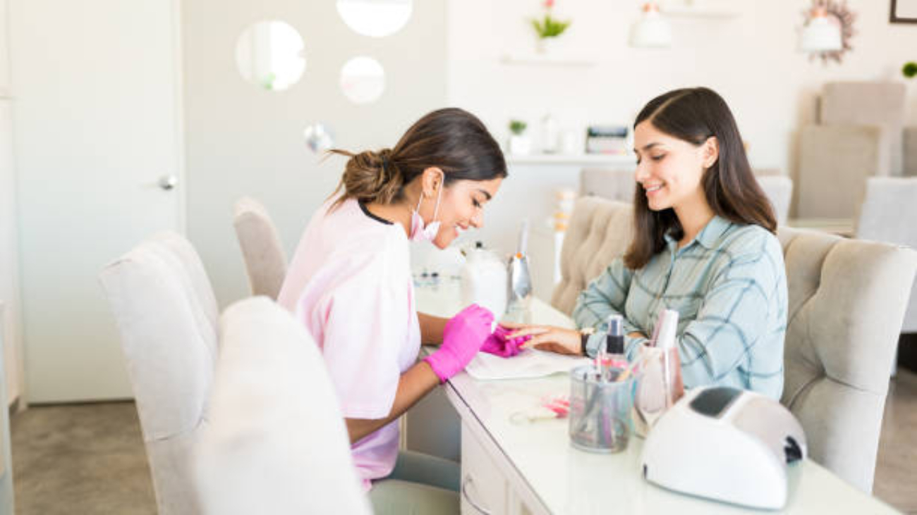 Smiling manicurist decorating nails with color on client's hand at beauty spa